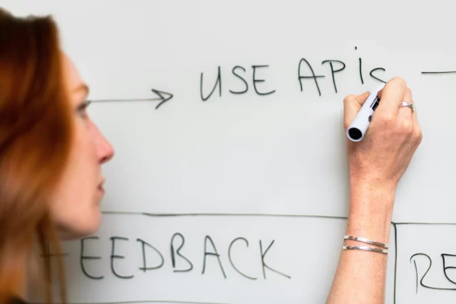 A woman writes "USE APIS" and "FEEDBACK" on a whiteboard to illustrate Healthcare Back Office workflow automation.