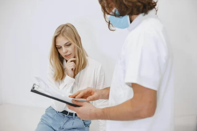 A healthcare professional in a mask reviews clinical notes with a patient during a Customer-Centric consultation.