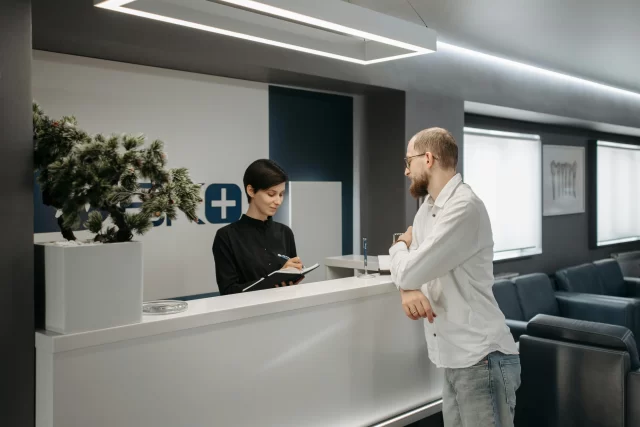 Receptionist assisting a patient at a medical facility, emphasizing a Customer-Centric approach to healthcare.