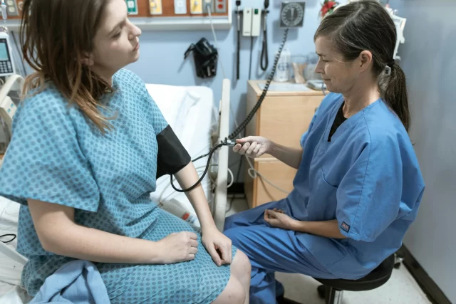 A nurse in scrubs measures a patient's blood pressure as part of comprehensive Care Coordination.