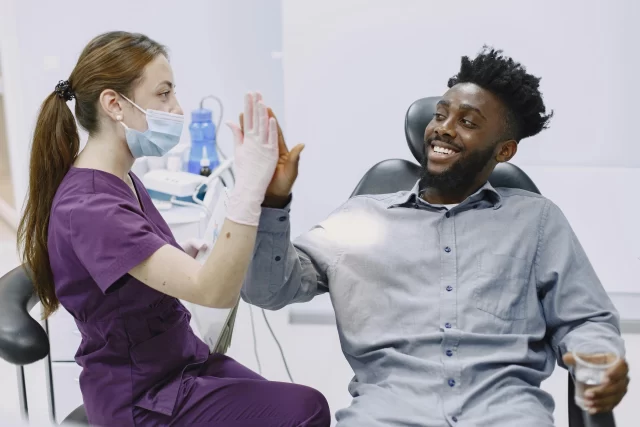 A female dentist giving a high-five to a smiling male patient, illustrating Patient Satisfaction in Healthcare.