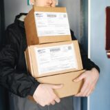 A person holding three stacked cardboard packages with USPS Express Mail labels, representing the home OptumRx delivery.