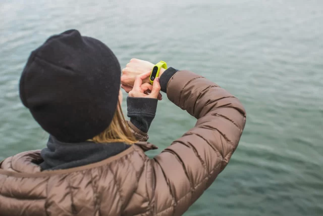 Woman in a winter jacket checking her fitness tracker to monitor her HIM Health metrics.