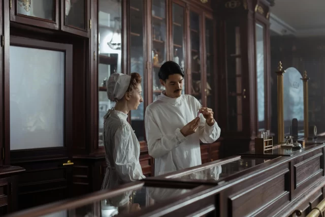 A male PMB and a nurse in period attire examining a chemical sample during research.