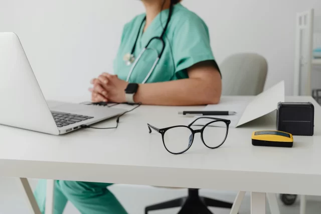 Medical professional at a desk with a laptop and eyeglasses, representing Healthcare Management Association operations.