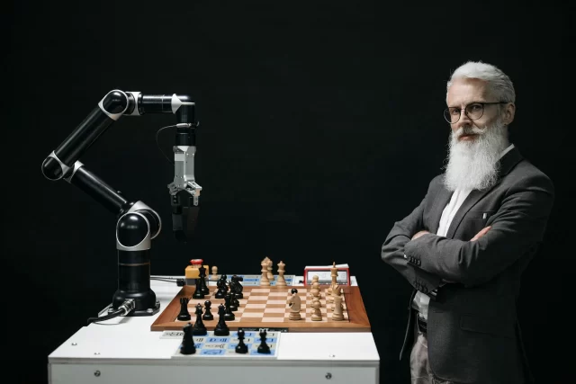 A white-bearded man plays chess against a robotic arm, symbolizing the evolution of Health Information Management technology.