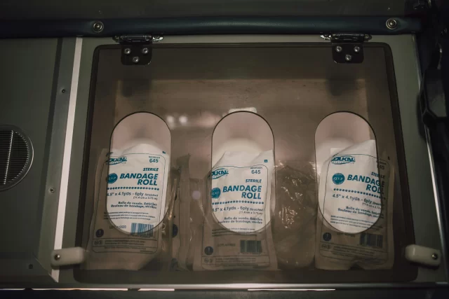 A clear dispenser cabinet containing three packages of Dukal sterile bandage roll DME.