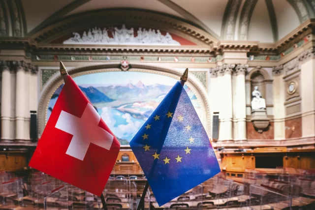 Flags of Switzerland and the European Union displayed in a legislative chamber to represent AI In Patient Support.
