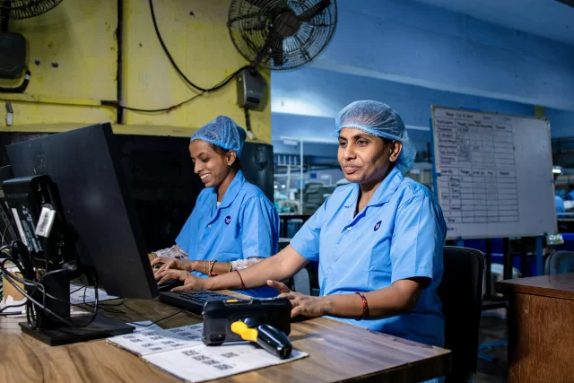 Two women in a factory setting monitor screens, tracking data for regulatory compliance updates EU.