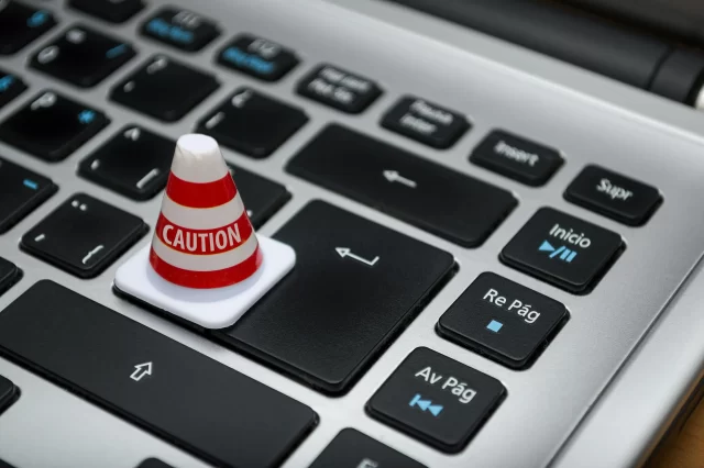 A miniature caution cone sits on a laptop enter key to symbolize risks within AI In Patient Support.