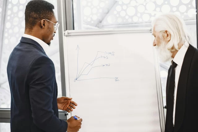Business professionals discussing Cost Reduction in Healthcare Operations while reviewing a growth chart on a whiteboard.