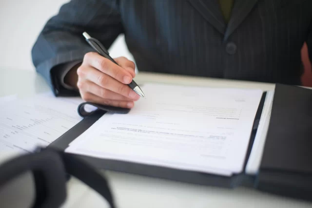 A business professional in a suit signing legal documents for an anonymous case study.