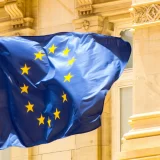 The European Union flag waving in front of a building, representing regulatory compliance updates EU.