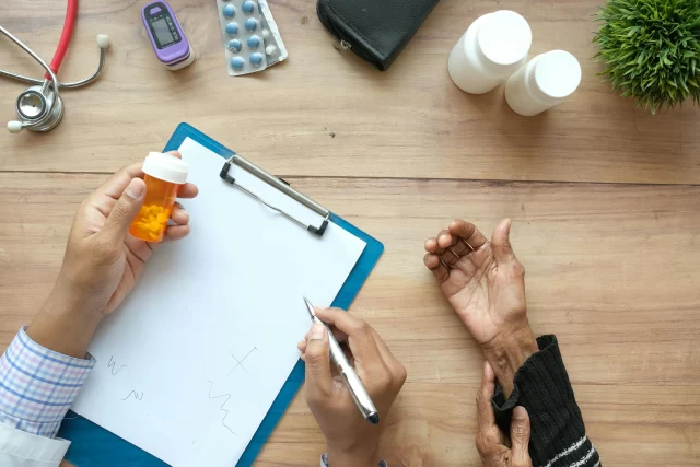 A pharmacist with a prescription bottle and clipboard consults with a patient, highlighting how Managers for pharmacy benefit streamline care.