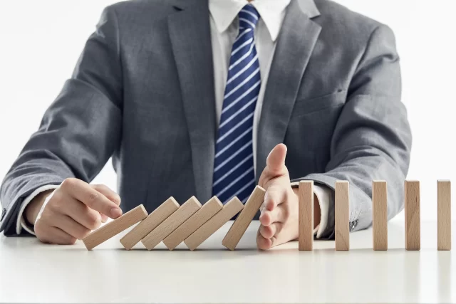 Business professional stopping a falling row of dominoes to illustrate risk management in Swiss Private Medical Insurance.