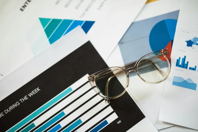 Eyeglasses resting on various business charts and data reports used for Health Info Management in Zürich.