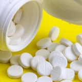White 200mg pills spilling from an open bottle, representing data points in a Swiss HEDIS chart.