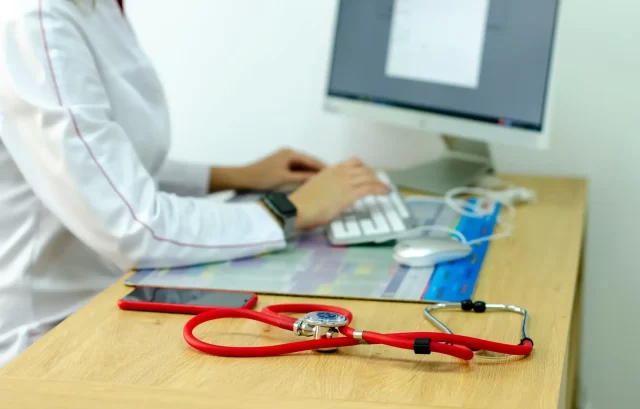 Doctor typing on a computer, facilitating remote patient care through Swiss telehealth services.