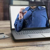 Doctor holding a stethoscope in front of a laptop screen, representing modern Swiss telehealth services.